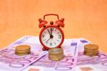 500 Euro Scheine, Münzen und kleiner roter Wecker. Bild: Pixabay
