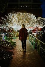 Frau läuft einen Weg entlang, der mit bunten Lichterketten beleuchtet ist. © Pixabay
