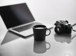 Laptop, Kamera und Kaffeetasse auf einem Tisch. Bild © pixabay