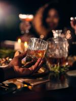 Hand hält Glas mit Whiskey vor unscharfem Hintergrund mit Flasche und Gesicht © pixabay